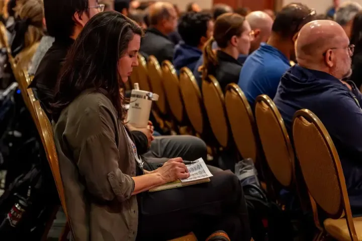 An attendee writing notes on her program during an All Things AI 2026 session